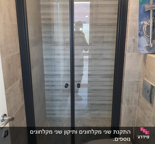 מקלחון זכוכית עם דלתות שחורות בחדר אמבטיה